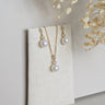 Pearl necklace and earrings set on a textured white card with dried flowers in the background.