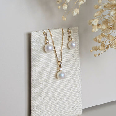 Pearl necklace and earrings set on a textured white card with dried flowers in the background.
