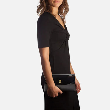 Woman wearing a black dress with a knot detail, holding a matching clutch against a white background