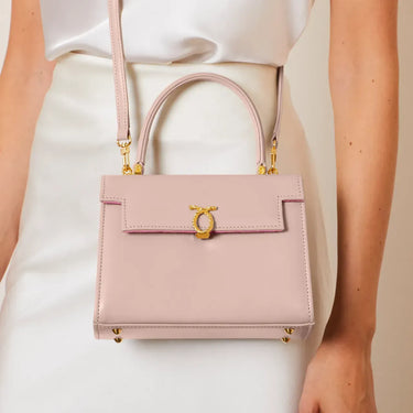 Pink handbag with gold accents held by a person wearing a white outfit.